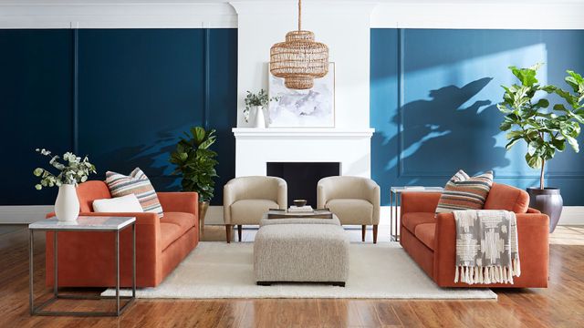 front view of a modern style living room with a bright orange sofa, blue walls, and white accents and chairs