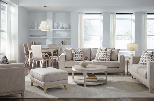 front view of a casual living room with light beige furniture including a sofa, chair, ottoman, coffee table, and dining table with chairs in the background
