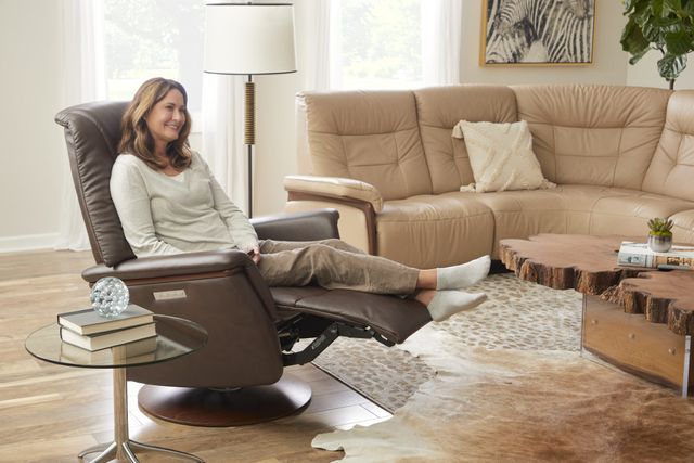 front view of a woman smiling and sitting in a stressless chair in a modern living room