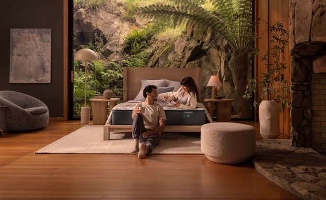 Front view of a bobo style bedroom with a man and woman having a cup of coffee on and next to their platform bed with mattress, respectively. 