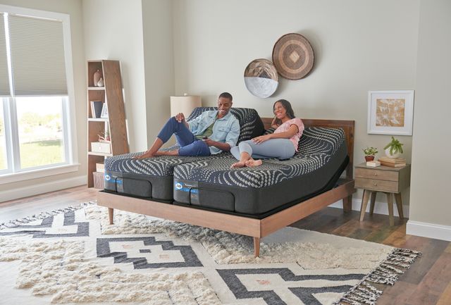 Front view of a man and woman sitting on a Sealy split mattress