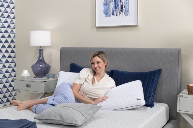 Front view of a woman sitting on a Sealy queen mattress