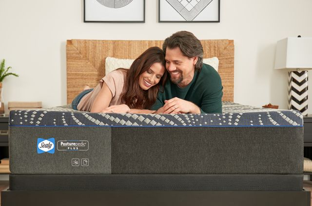 front view of a couple sitting on a sealy mattress