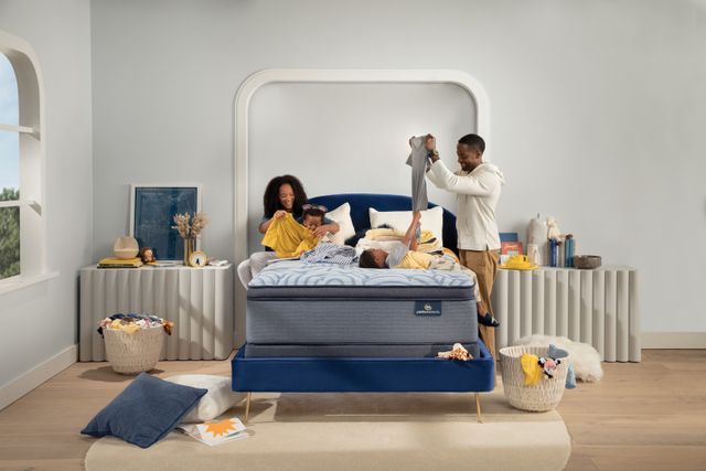 front view of a family with two parents and two children folding laundry sitting on and standing around a pillow top mattress