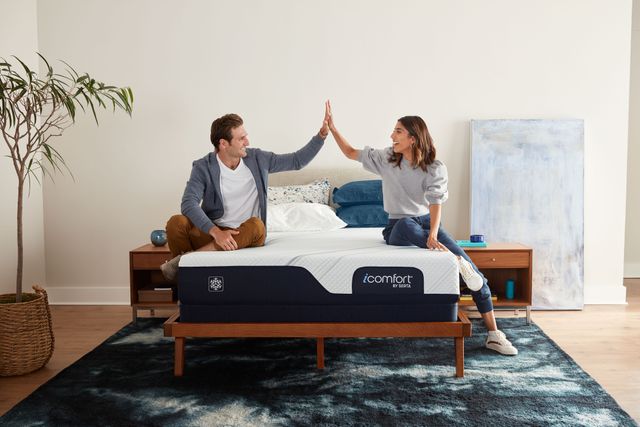 front view of a man and woman sitting on opposite sides of a serta mattress high-fiving