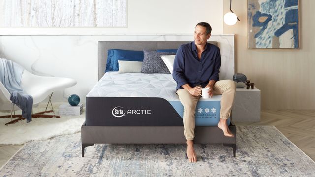 front view of a man sitting on the edge of a Serta mattress in a modern bedroom