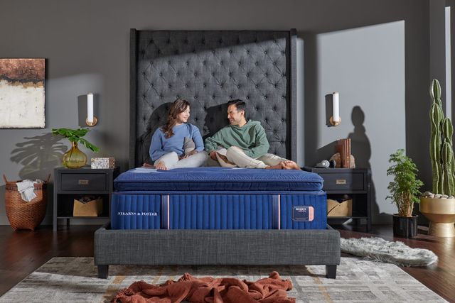 front view of a man and woman sitting on a Stearns and Foster mattress in a contemporary bedroom