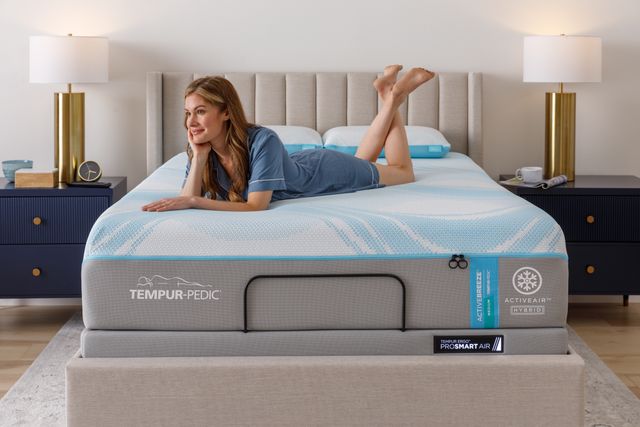 Front view of a woman laying on her stomach on a Tempur-Pedic mattress and smiling.