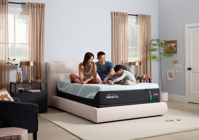 Front view of a modern bedroom with a mother and father smiling and playing with their son and his toy truck on a hybrid mattress
