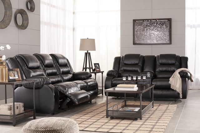front view of a black leather reclining loveseat and with various contemporary decor