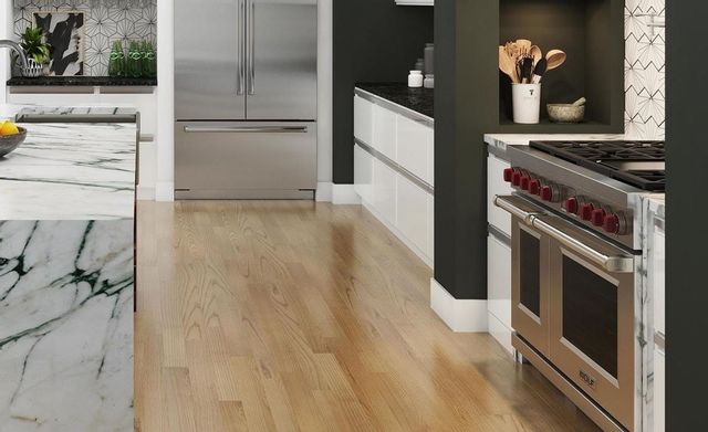 side view of a modern contemporary kitchen with a french door refrigerator in the front and a wolf range on the right in the white and black counters