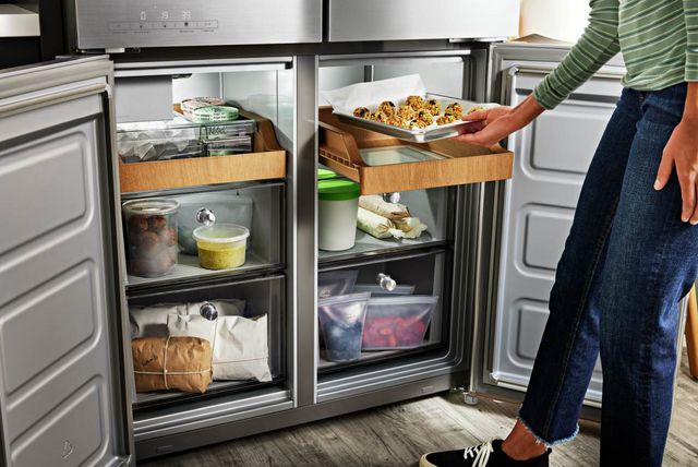 front view of the lower half of a four door refrigerator with both doors open and a person putting cookies in a drawer of the right side