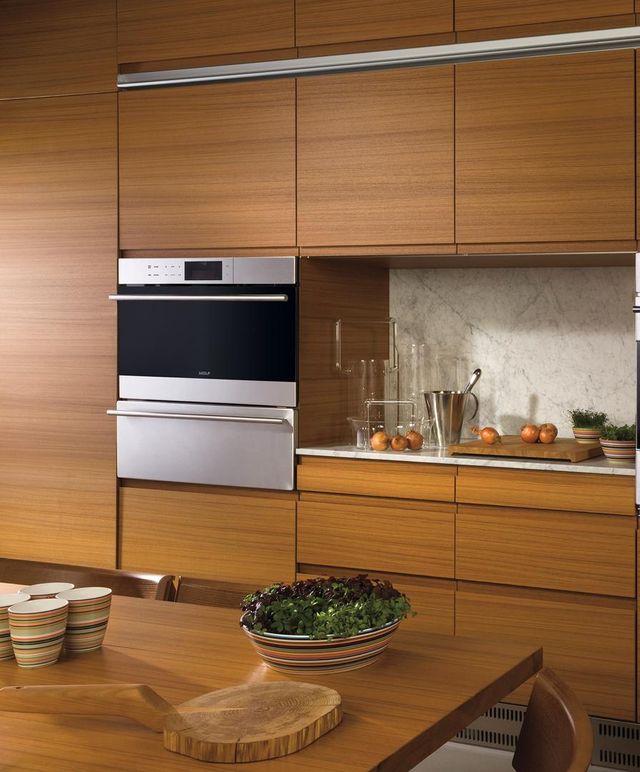 A Wolf steam oven and warming drawer are featured in a mid-century modern kitchen with natural wood cabinets
