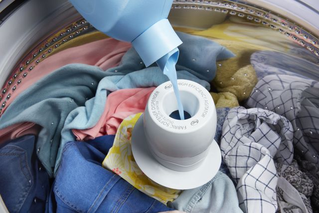 washer full of clothes with agitator being filled with laundry detergent
