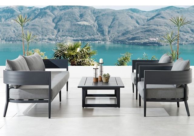 side view of an outdoor sofa, two matching chairs and table on an outdoor patio with a bay and mountain in the background