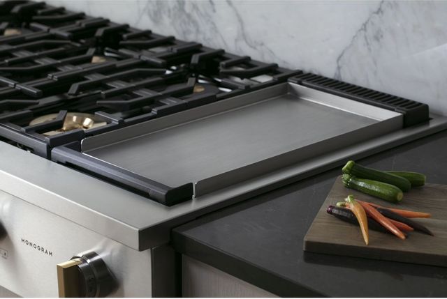 closeup view of a monogram rangetop with grate and some veggies on a cutting board on the countertop beside it