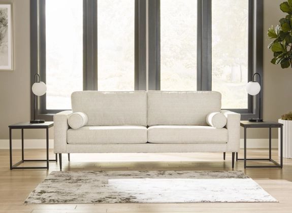 front view of a contemporary cream sofa in a modern room in front of large windows with two simple black side tables on either side