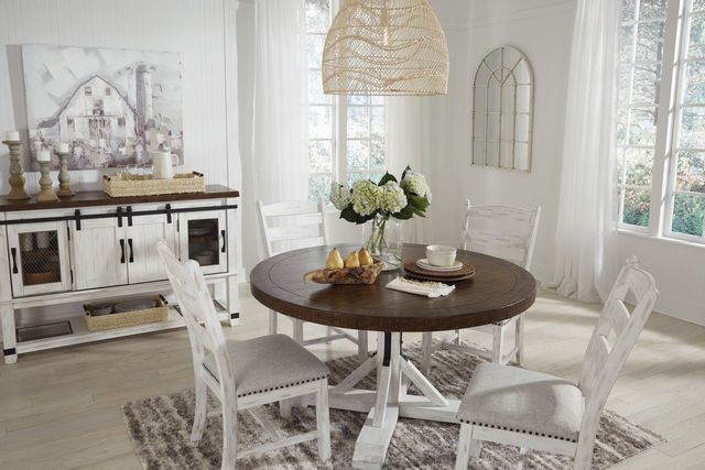 standing view of a farmhouse dining room with a round pedestal dining table, matching chairs, and a matching side table