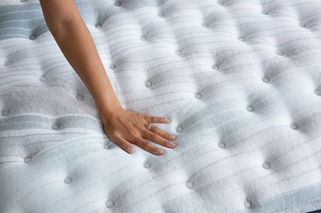 view of an arm pressing down on a white mattress 