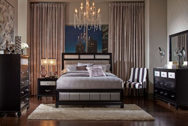 front view of a dark luxury bedroom with long pink curtains and black furniure, and a large chandelier hanging above the bed