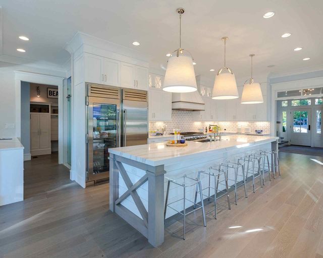 front left angled view of a white luxury kitchen with a stainless steel column refrigerator and freezer