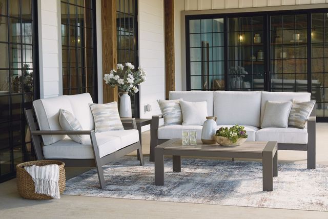 Front view of a grey outdoor sofa with a matching chair and table on an outdoor patio with large windows in the background