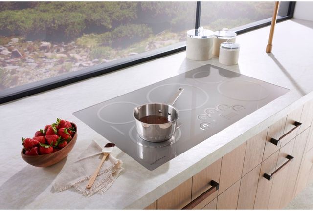 top view of a gray monogram cooktop with chocolate melting in a pan and strawberries next to it on the counter