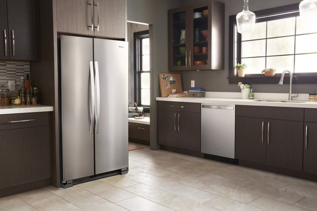 whirlpool-header modern kitchen with brown cabinets and a whirlpool side-by-side refrigerator, sink, and cutting board.