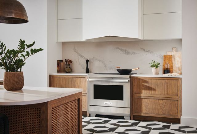 front view of a boho style kitchen with a wolf induction range in front of a marble backsplash between light wood cabinets