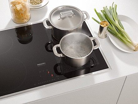 Two pots boil water and cook food atop a stainless steel cooktop