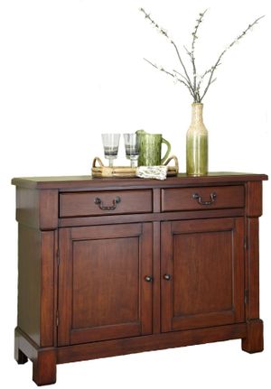 homestyles brown wood dining buffet styled with a serving tray, a green water pitcher, glasses, and a vase