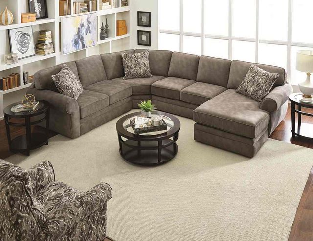 front tall view of a modern living room with a brown sectional chaise sofa, a bookshelf wall in the background, and decor througout
