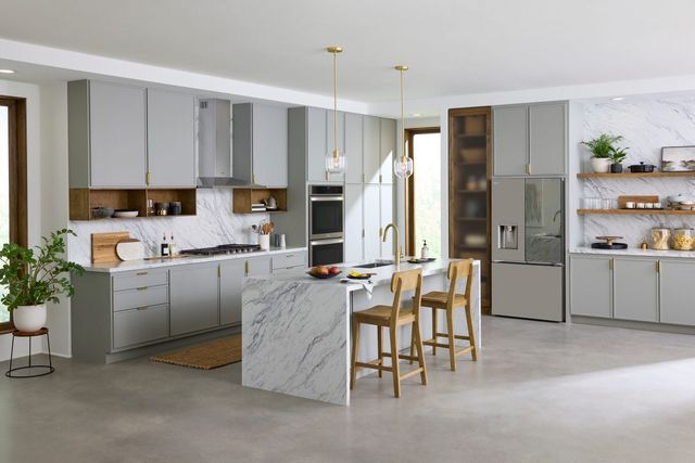 view of a modern white kitchen with a marble waterfall island and a smart refrigerator built into the cabinets