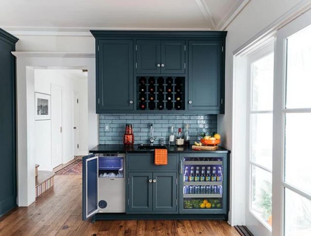 front view of a kitchen with dark green cabinetry and white walls, with an ice maker installed in the cabients