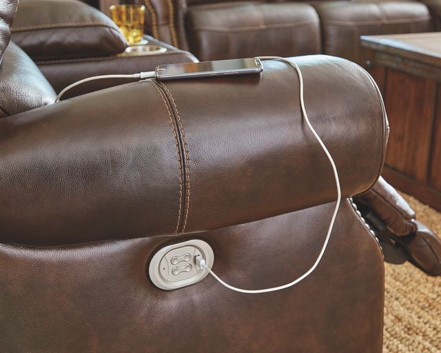 A USB outlet charges a phone on a brown leather reclining sofa