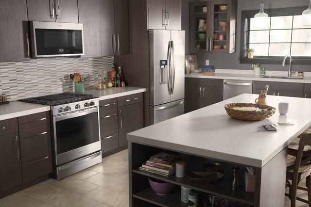 Stainless steel Whirlpool appliances are installed in a kitchen with dark brown cabinets
