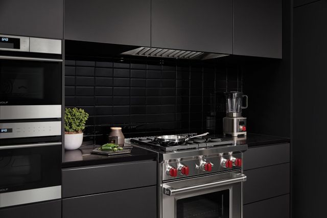 front view of a wolf range and two wall ovens in a minimalist dark kitchen