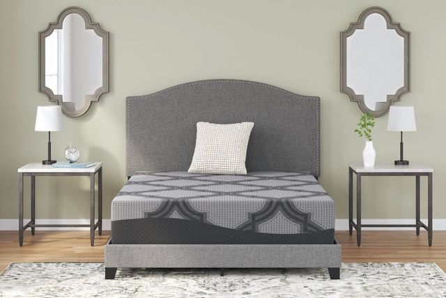 front view of a mattress on a grey bed frame, with a side table and wall mirror on both sides of the bed