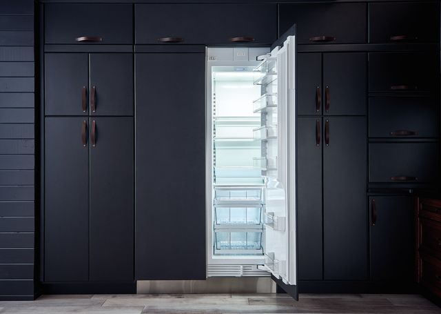 front view of a dark blue wall of cabinets with an open column refrigerator showing the lit up inside