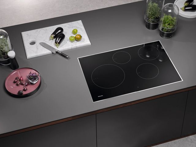 top view of a grey counter with a black miele induction cooktop surrounded by cooking ingredients and tools
