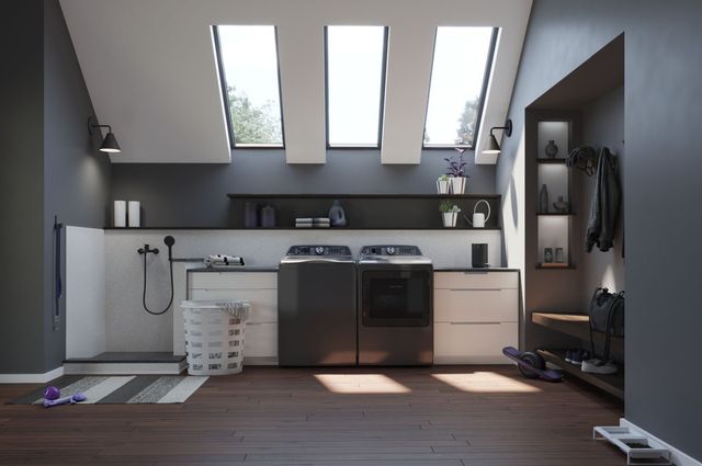front view of a gray laundry room with a black washer and dryer in the middle  of white cabinets