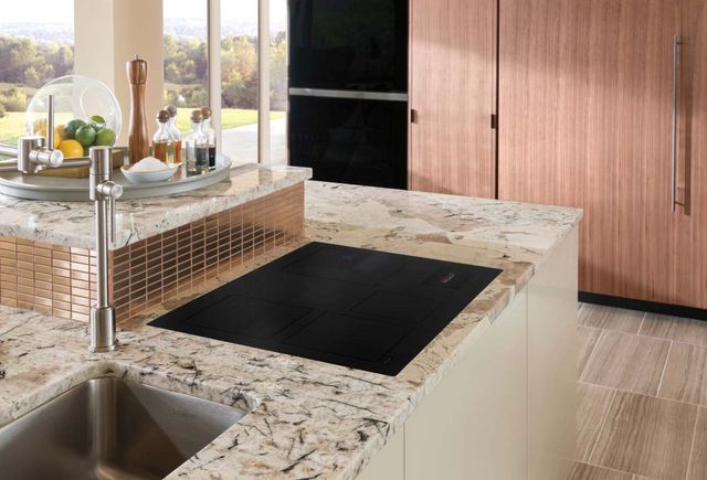 cooktop built info kitchen counter. Kitchen is light pick marble and light wood, stylized with a copper backsplash and a bowl of lemons and limes