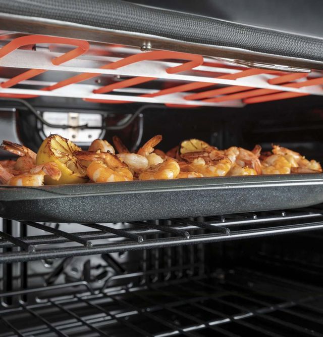 A metal tray with seafood is broiled beneath an oven's heating coil
