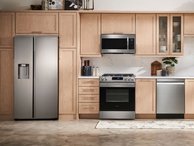 front view of a modern kitchen with light wood cabinetry and a side by side counter depth refrigerator with matching appliances throughout