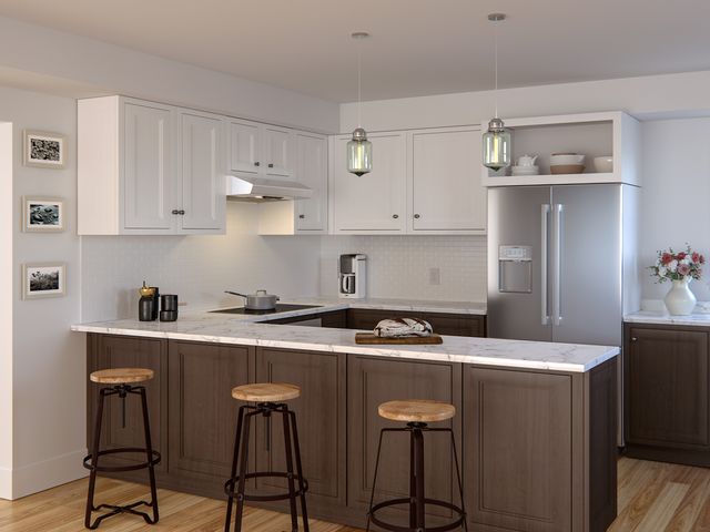 kitchen with white walls and cabinets, white marble countertops, and dark wood panel coffee bar with three round barstools. Kitchen features a ductless range hood and refrigerator