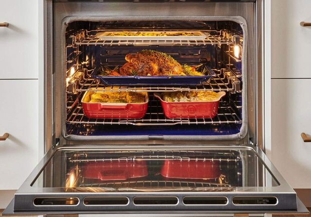 front view of an opened wolf oven with a turkey and two side dishes inside