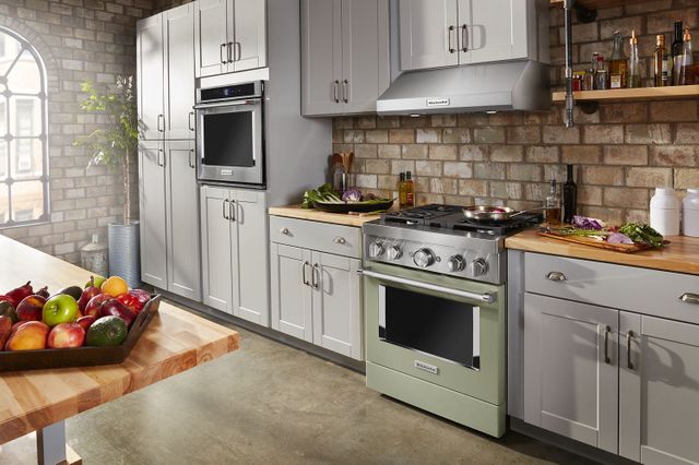 view of a farmhouse style kitchen with gray cabinets, light stone walls, and a sage green kitchenaid professional range
