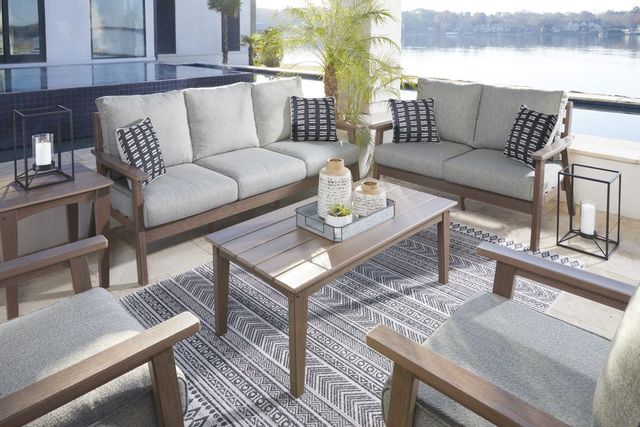 standing view of a beige outdoor sofa, matching loveseat, two chairs, and a coffee table on a back deck with the ocean in the background