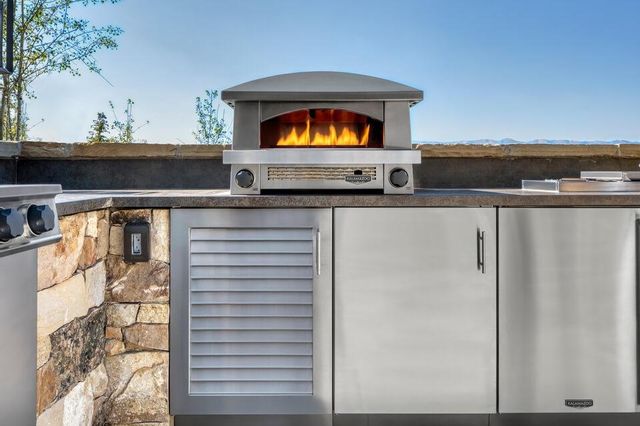 front view of a modern outdoor cooking area with an outdoor pizza oven on top of the counter and outdoor refrigerators below