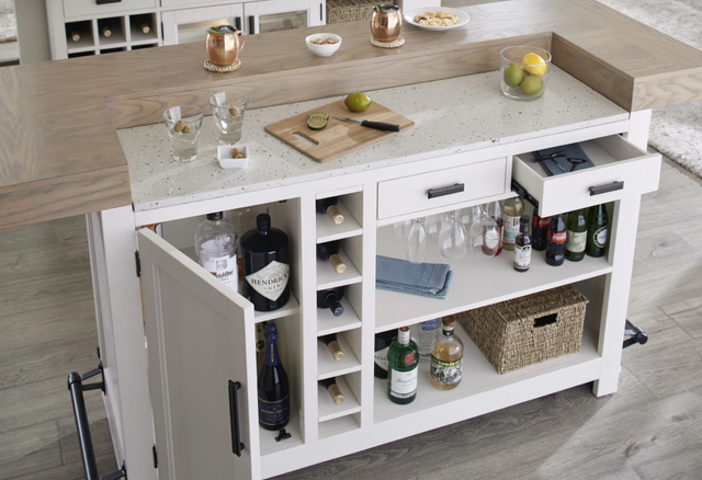 standing view of a white home bar with various drinks, bottles, and glasses in the storage compartments, as well as two drinks and a lime garnish on the bar top
